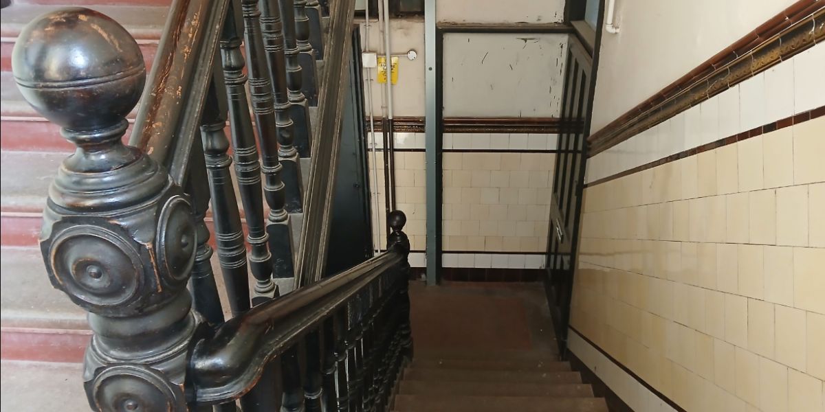 A Victorian Tenament stairway with a carved wooden banister and cream and brown wall tiles