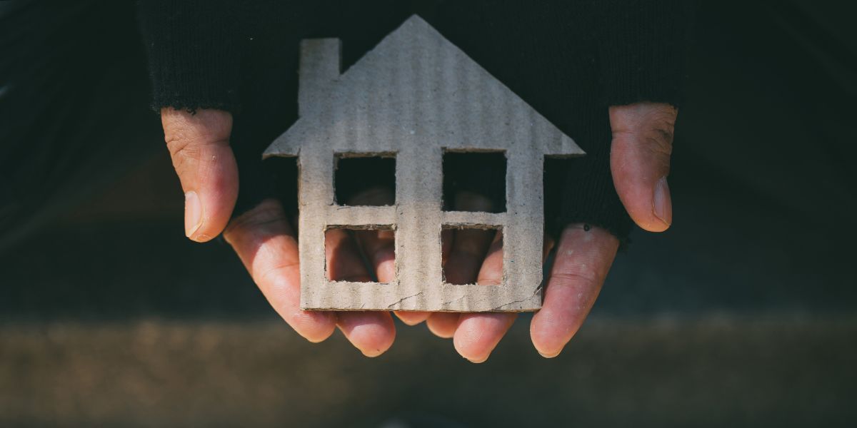 Hands in woolen, fingerless gloves cradle a cardboard cutout of a house