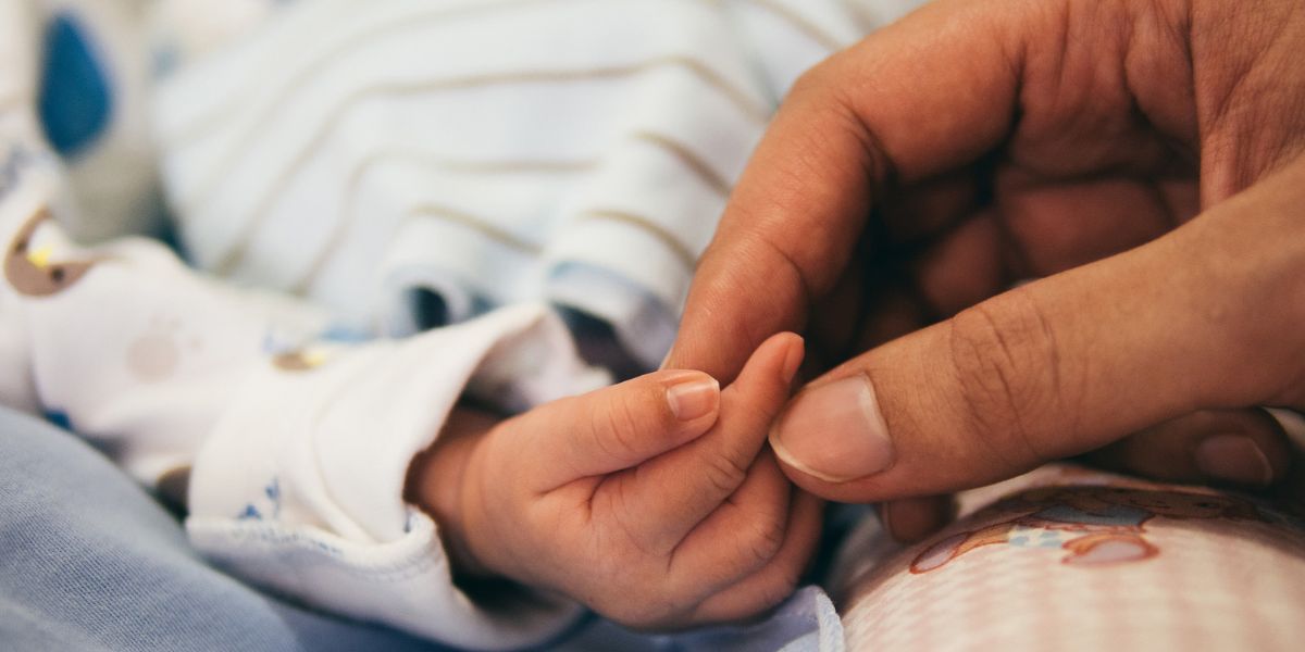 adult holds the hand of a small baby wrapped in blankets