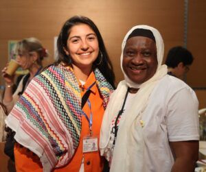 Two smiling women, one wearing a keffiyeh, the other with a white hijab