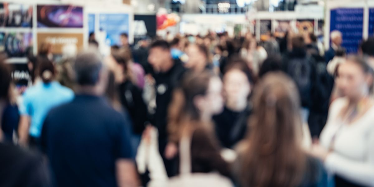 Out of focus photograph showing large groups of people milling about an open conference space