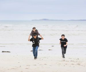 Three smiling children run along a sandy beach on the Isle of Lewis